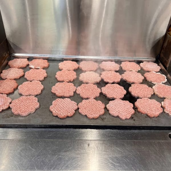 Rows of burger patties cooking on a large commercial griddle, with steam rising.