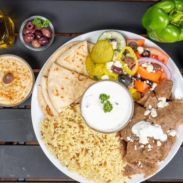 A gyro platter with meat, rice, pita, salad, hummus, and tzatziki, with olive oil and olives.