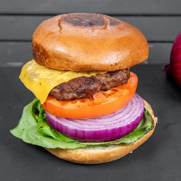 A cheeseburger with lettuce, tomato, and red onion on a dark surface, with a whole red onion beside it.