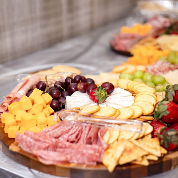 Round charcuterie board with salami, cheddar, brie, grapes and crackers