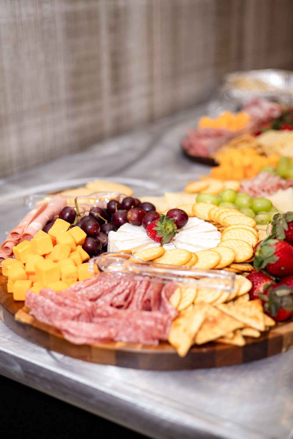 Round charcuterie board with salami, cheddar, brie, grapes and crackers