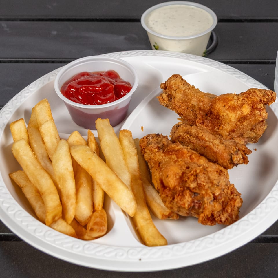 Fried chicken wings and french fries with ketchup and ranch dressing on a white plate.