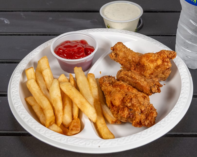 Fried chicken wings and french fries with ketchup and ranch dressing on a white plate.