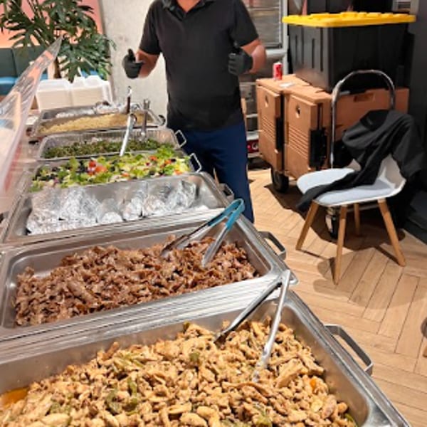 Caterer gives thumbs-up behind a buffet line with multiple hot and cold food dishes.