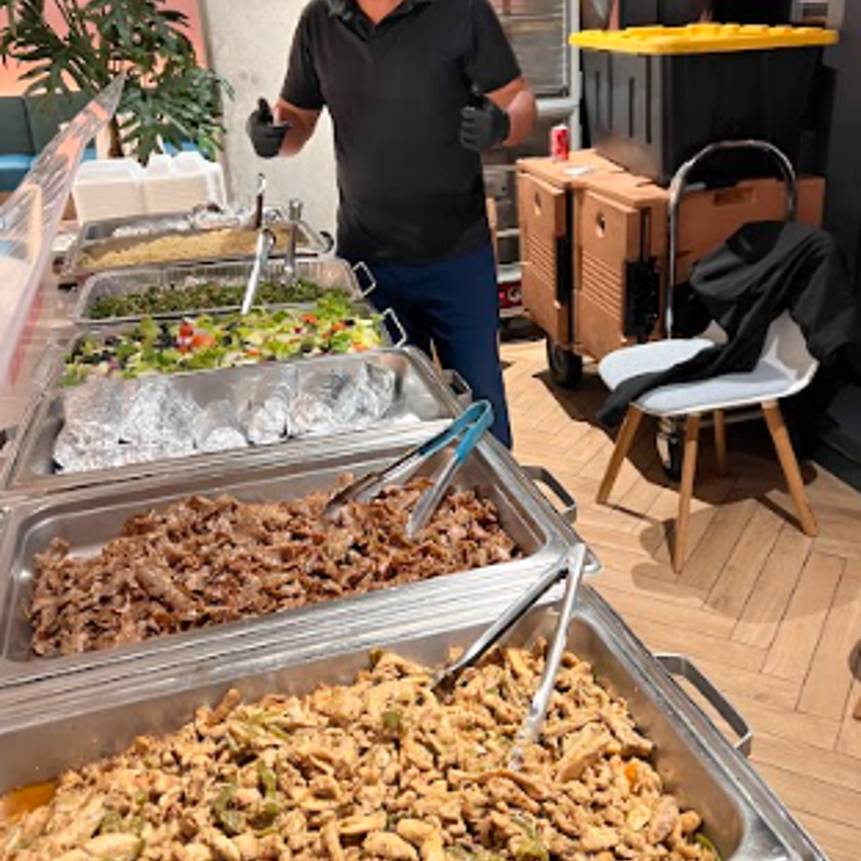 Caterer gives thumbs-up behind a buffet line with multiple hot and cold food dishes.