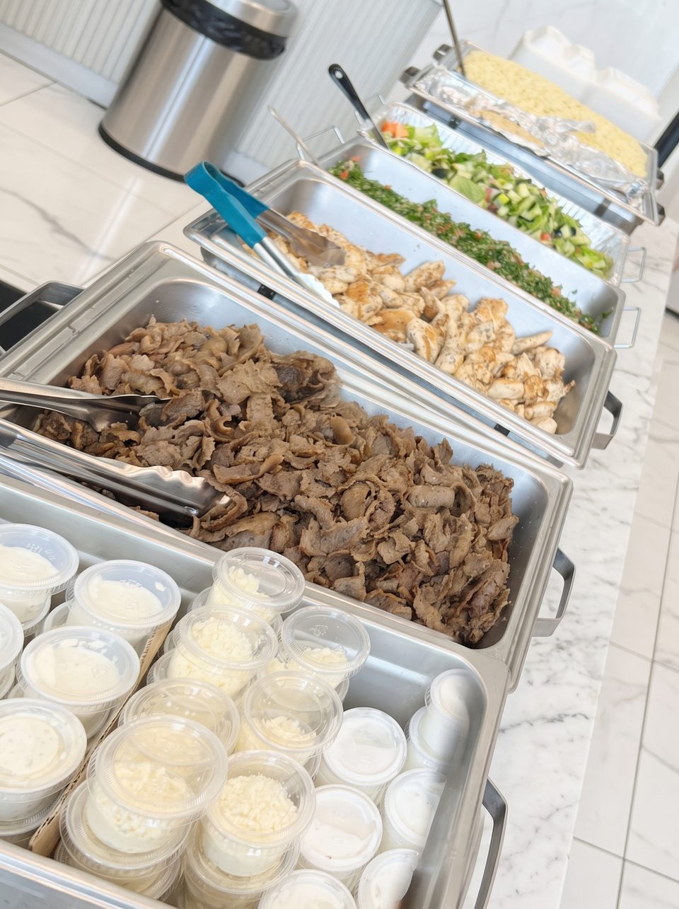 Catering spread with gyro meat, grilled chicken, salads, tabouli, and sauces
