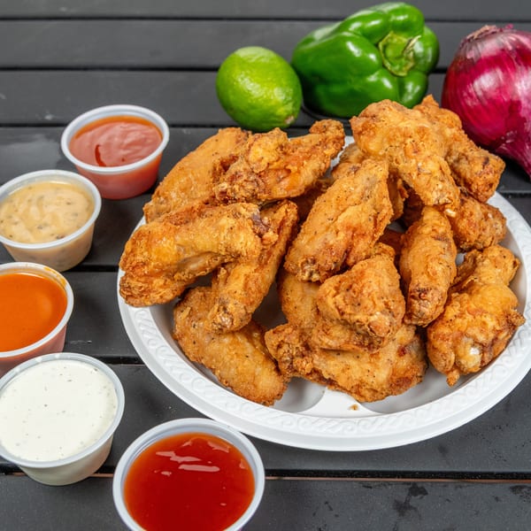 Crispy fried chicken wings on a white plate, surrounded by various dipping sauces and fresh vegetables.