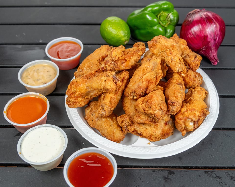 Crispy fried chicken wings on a white plate, surrounded by various dipping sauces and fresh vegetables.