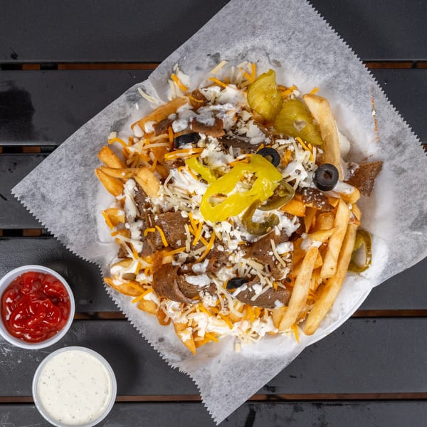 Loaded fries with gyro meat, cheese, olives, peppers, and sauces on a dark table.