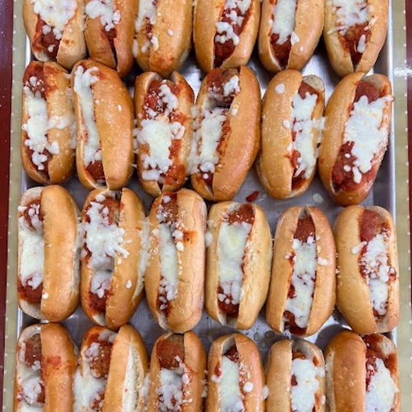 Numerous mini meatball subs with marinara sauce and melted mozzarella cheese on a metal tray.