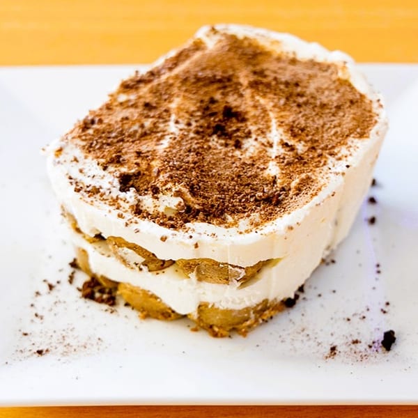 A slice of tiramisu dessert with layers of cream and cake, topped with cocoa powder.
