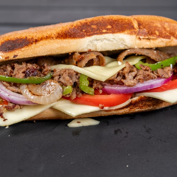 A close-up of a loaded cheesesteak sandwich with steak, cheese, peppers, onions, and tomatoes.